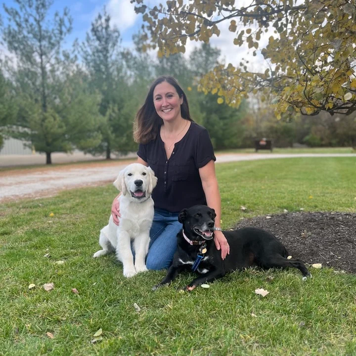 Dr. Christine Slagel sitting outside on the grass with two dogs.